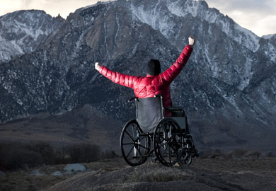 Person im Rollstuhl vor einer Bergkulisse